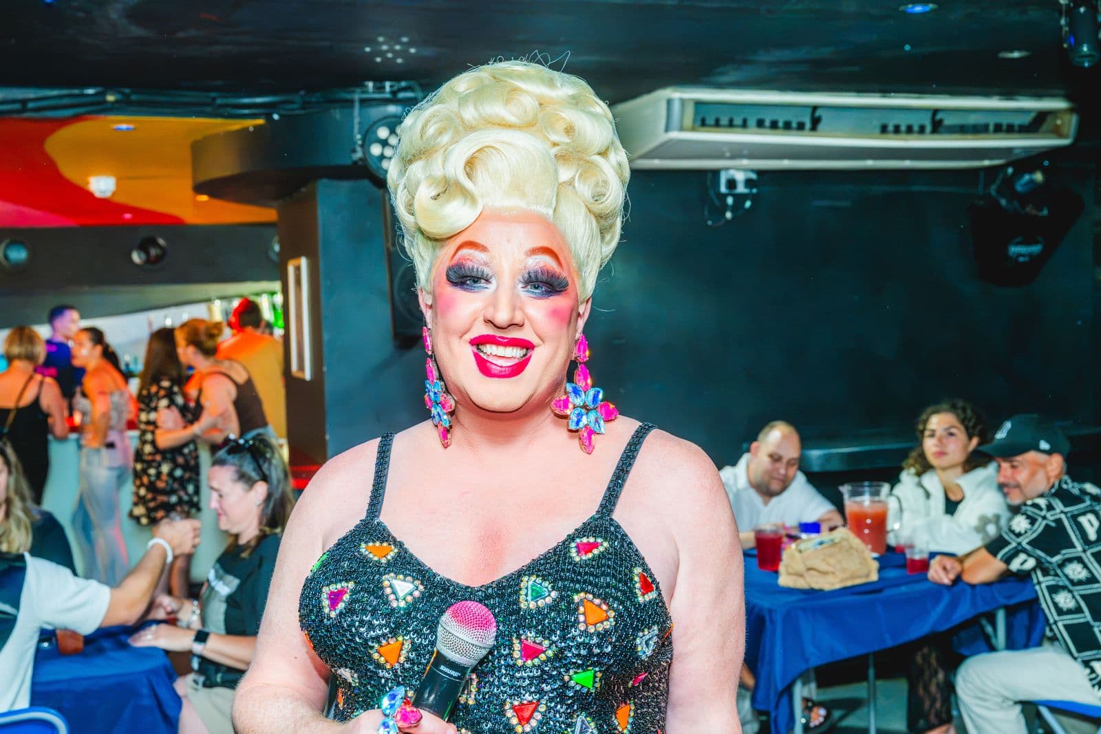 A drag queen with a big blonde beehive smiling at the camera